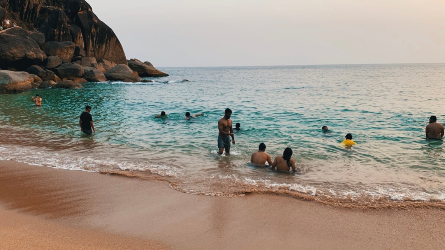 Swimmers floating near dark rocks at Butterfly Beach